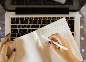 Female student writes in a notebook while using her laptop