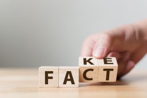 Wooden blocks spell out "fact" but a hand turns them to spell "fake"