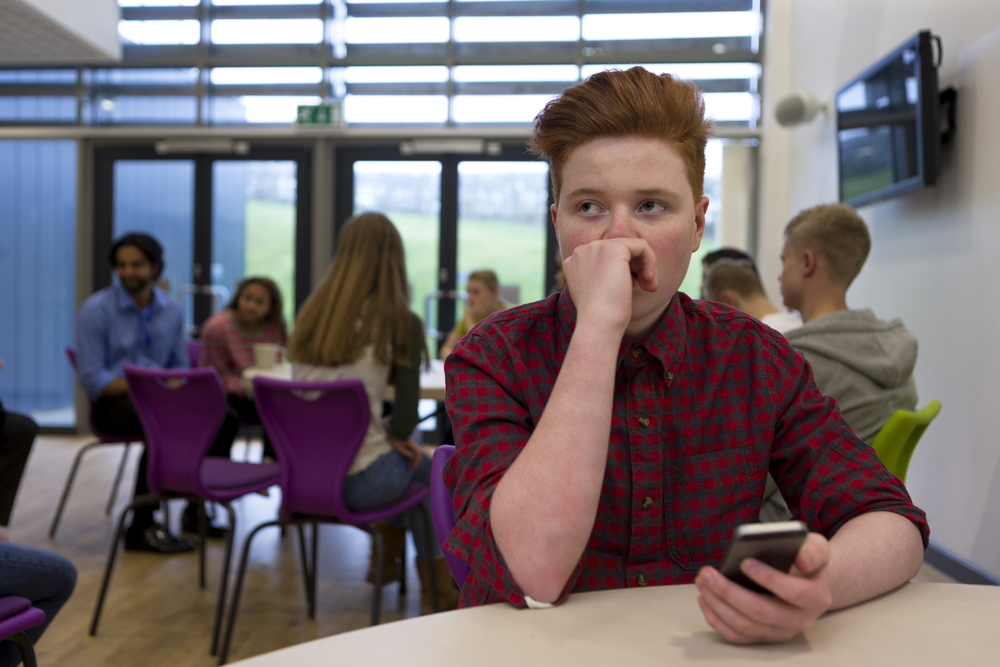 Nervous boy in cafeteria, phone in hand.