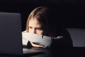 Sad teen girl in dark on computer.