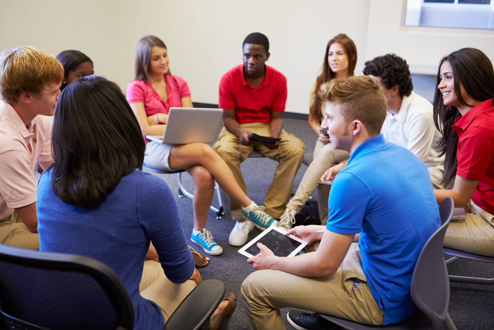 Teens in circle talking with laptops.