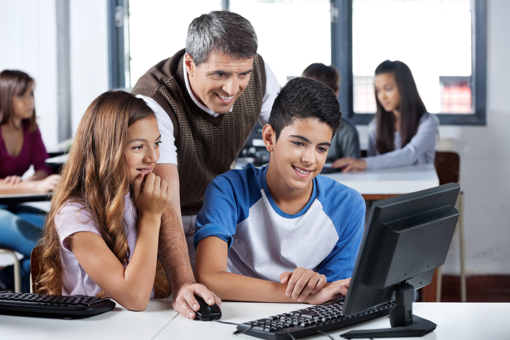 Administrator helps happy students with computer.