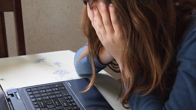 sad child covers face in front of computer.