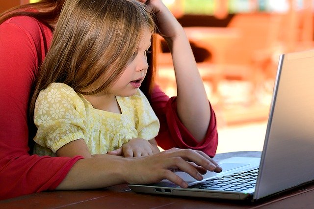 Little girl sits in mother's lap and looks at computer.