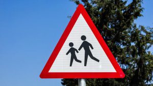 Triangular school safety sign with two figures running on a white field bordered in red.