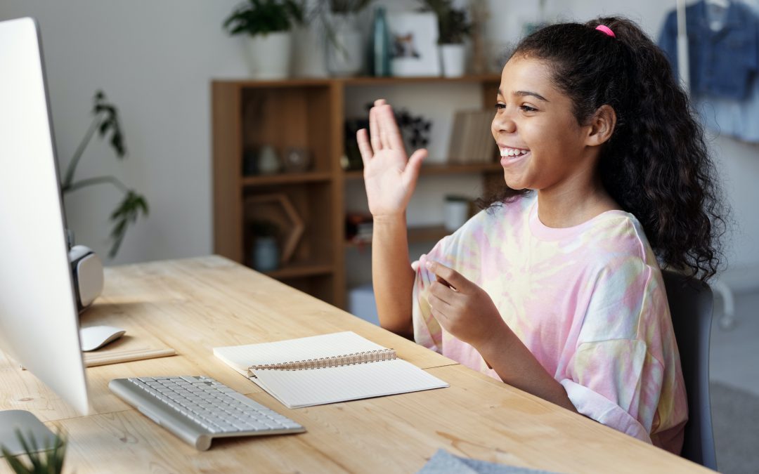 Young girl raises hand at computer while distance learning.