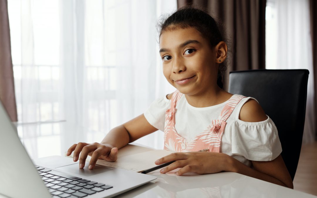 Young girl using laptop looks at camera and smiles.