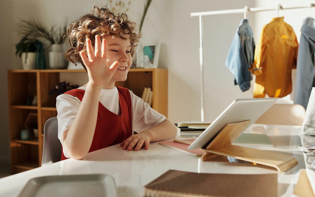 Smiling girl waves at online classmates.