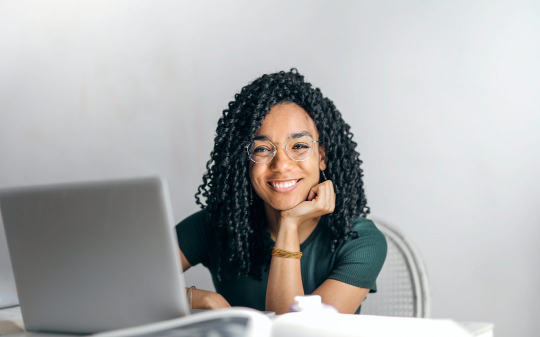 Teenage girl working at computer looks at camera and smiles.