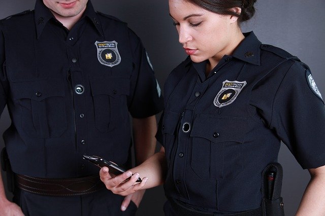A male and a female police officer look at a cell phone screen.