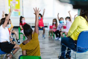 Classroom of children raising hands.
