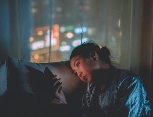 Sad Asian American teen looks at smartphone in a dark room.