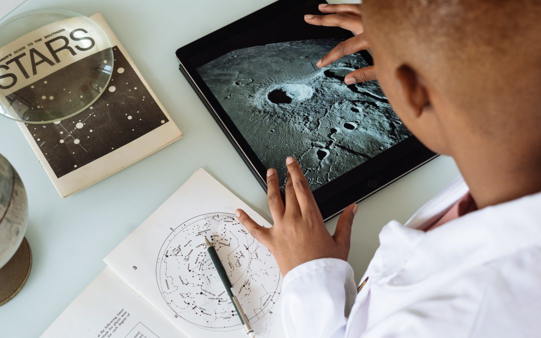Young Black student looks at surface of moon on an iPad.