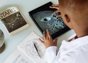 Young Black student looks at surface of moon on an iPad.