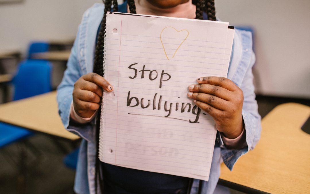 Girl in classroom holding up notebook with "Stop bullying" written on one page.