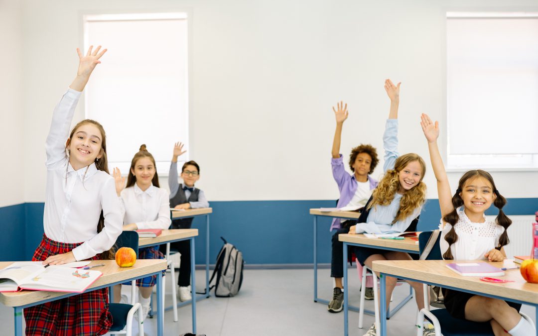 Happy students in desks raising their hands.