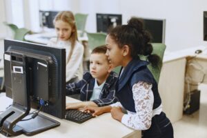 A boy and a girl work together on a classroom computer.