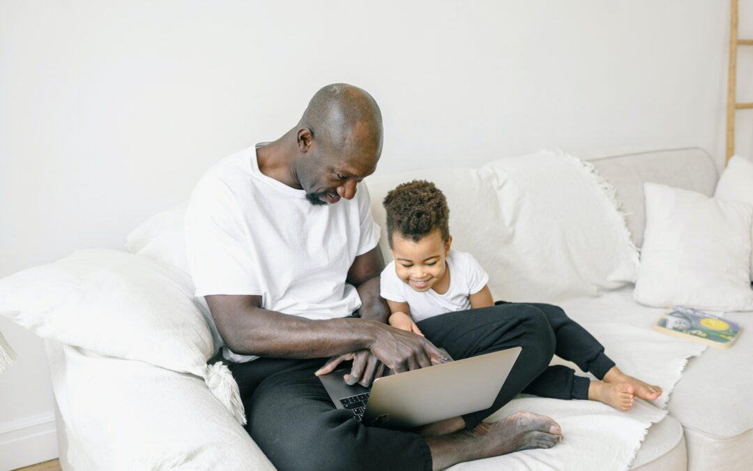 African American father teaches his young son how to use the computer.