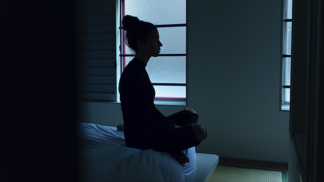 Silhouette of sad teenage girl sitting cross-legged on her bed in front of the mirror.